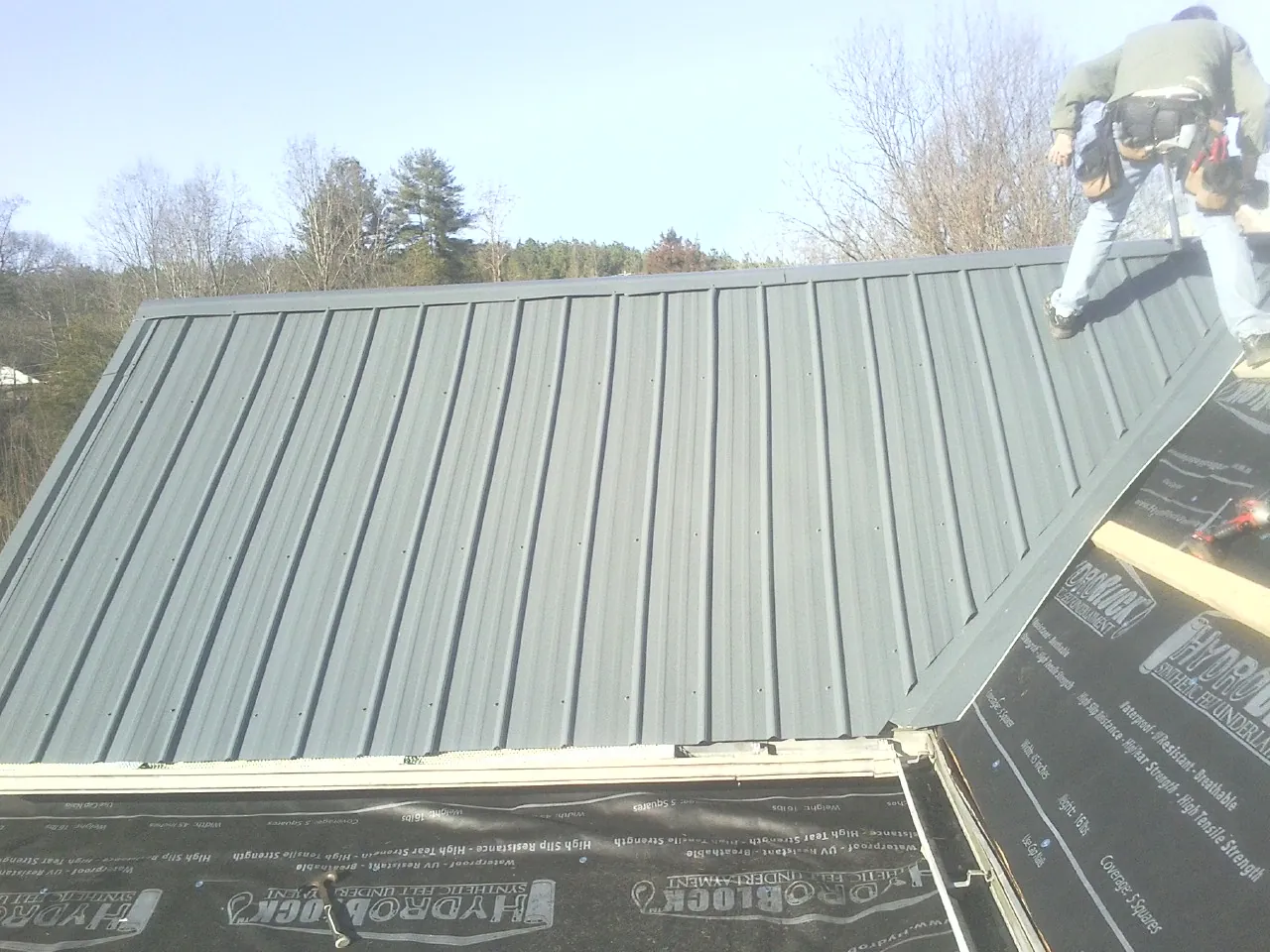 Crew installing dark green standing seam panels over synthetic underlayment in Navasota