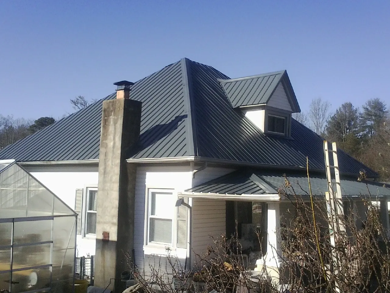 Dark blue standing seam metal roof on a white farmhouse with dormer — Slate & Tile Roof Repair by Roofing Brothers in Navasota