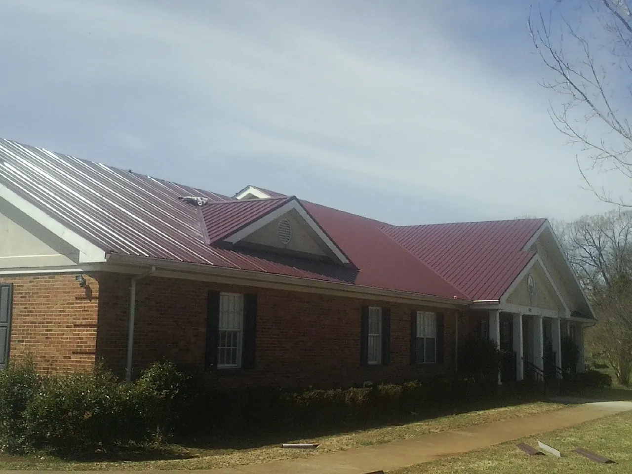 Red metal roof with gabled entries on a long brick building, from a Hail Damage Roof Repair job in Navasota