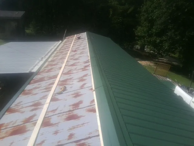 Old rusted panels beside newly installed green metal roofing — Wind Damage Roof Repair by Roofing Brothers in Navasota