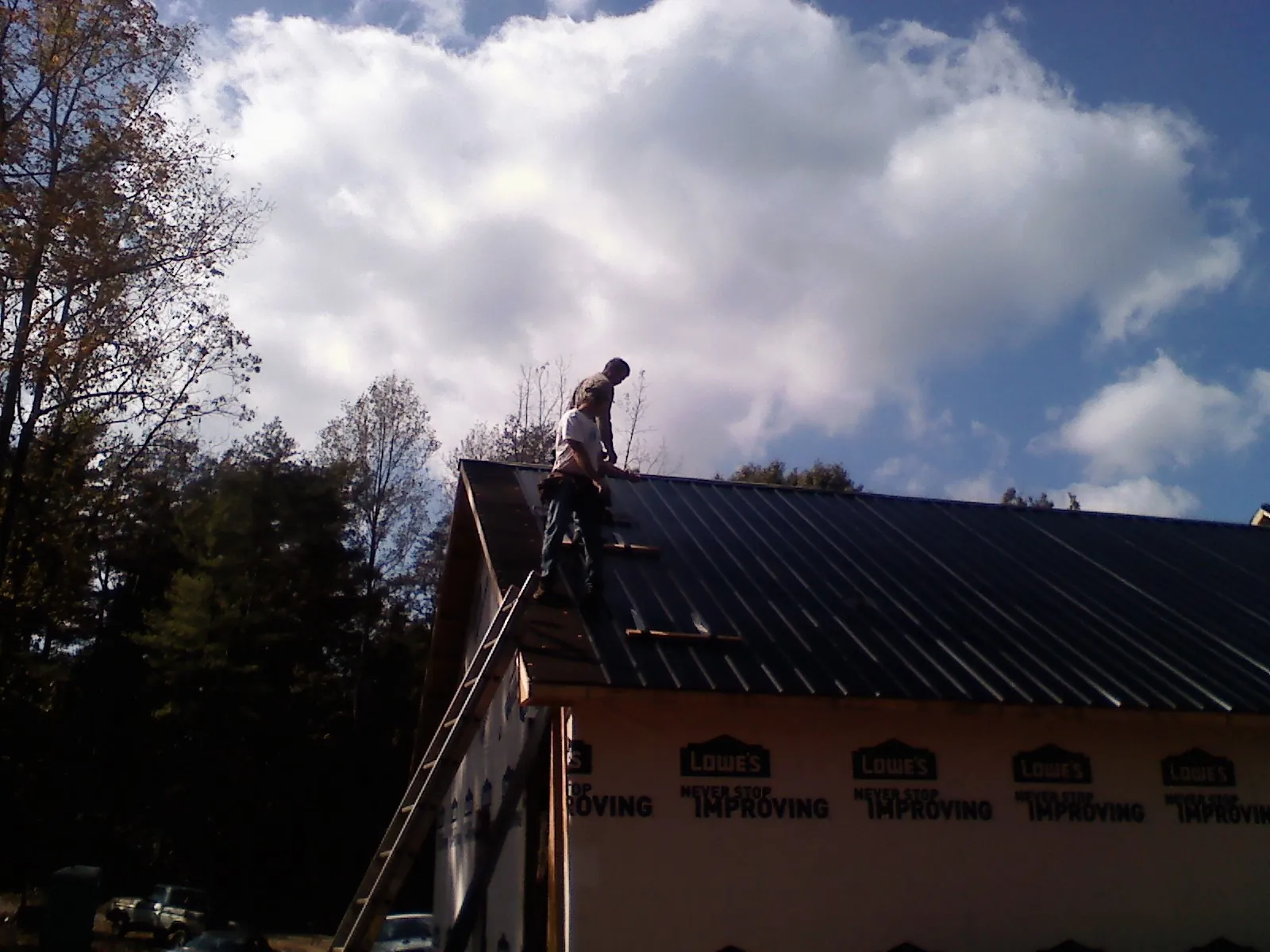 Roofer fastening dark metal panels high against a cloudy sky, from a Roof Inspection job in Navasota