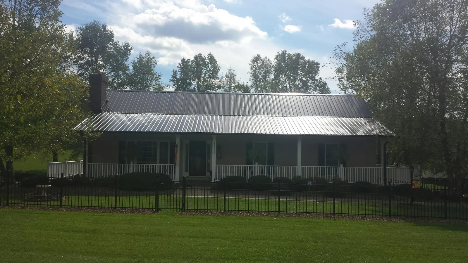 Gray metal roof on a brick ranch with a full width front porch — Gutter Guard Installation work by our crew in Navasota